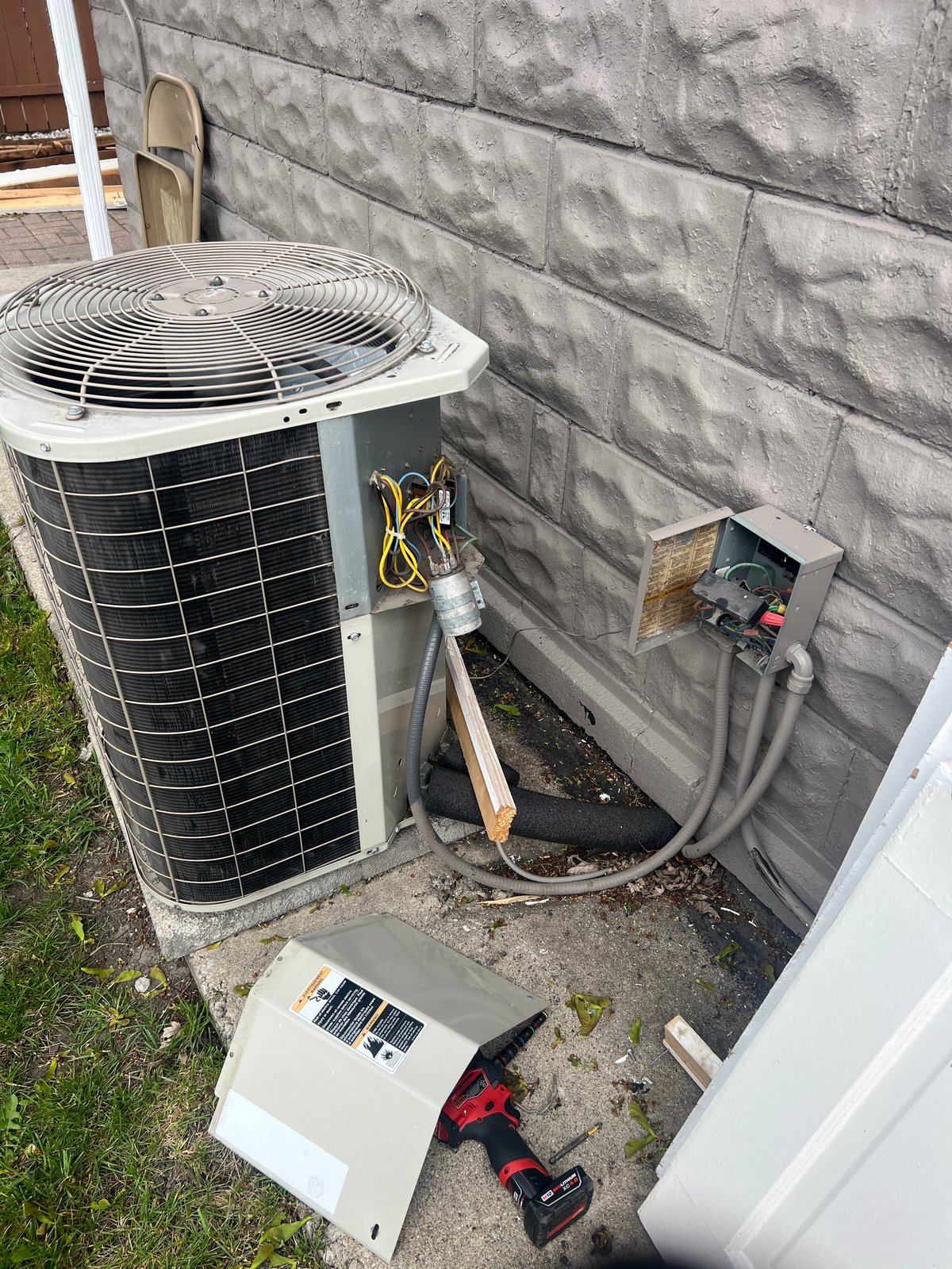 Outdoor HVAC air conditioning unit mounted on concrete foundation with condensate pump and electrical connections visible