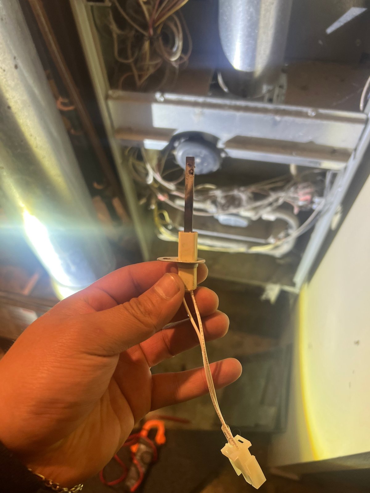 Hand holding a small tan and black electrical connector or sensor component in front of an appliance interior with metal parts visible